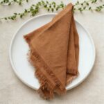brown cotton fringe napkin folded on white plate, rustic table setting
