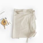 Half Linen Style Simple Apron light beige lifestyle flat lay, 100% washed cotton faux linen half waist apron for home baking and coffee shop
