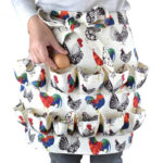 Rooster Print Canvas Egg Collecting Apron hand putting egg into ruffled pocket closeup