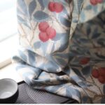 close shot of botanical print on cottage blackout curtain panel, blue branches and red berry pattern on white background