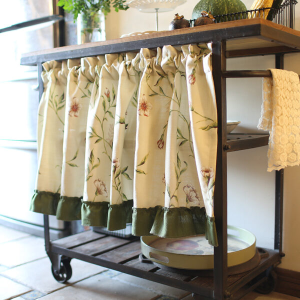Country‑style kitchen interior decorated with botanical print tier curtains