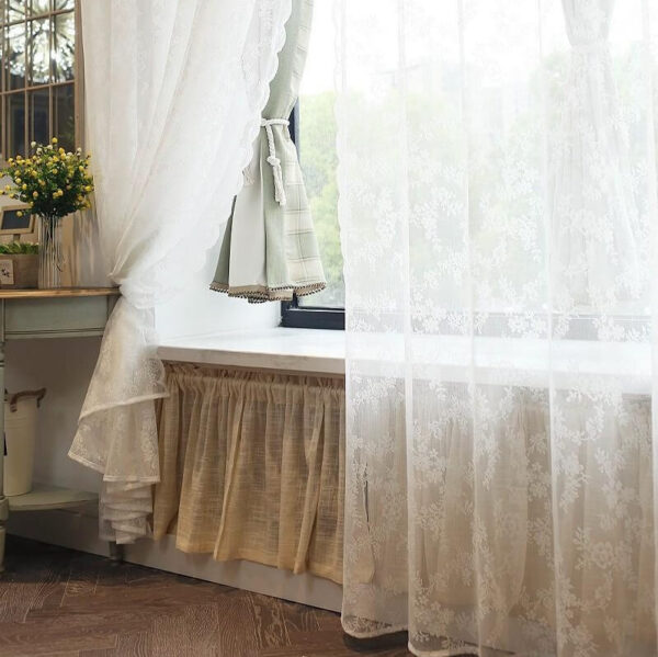 Romantic sheer white lace doorway curtain beside bright window with floral decor