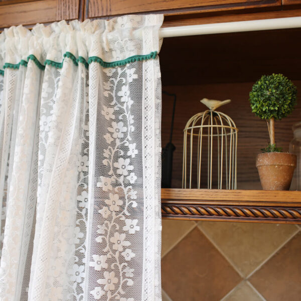 Light‑filtering white sheer door curtain with dark‑green trim for kitchen storage opening