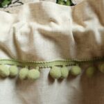 Close‑up view of linen‑texture curtain fabric and green pom‑pom fringe trim