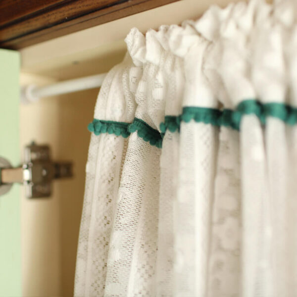 Close‑up of dark‑green header trim on white sheer door curtain, rod‑pocket top detail