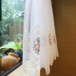 Close‑up view of rose floral embroidery on sheer tier curtain, delicate lace hem
