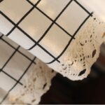 Close‑up of linen‑texture black grid curtain fabric, crochet lace trim detail