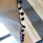 Close‑up view of black pom pom tassel edge on striped linen curtain panel