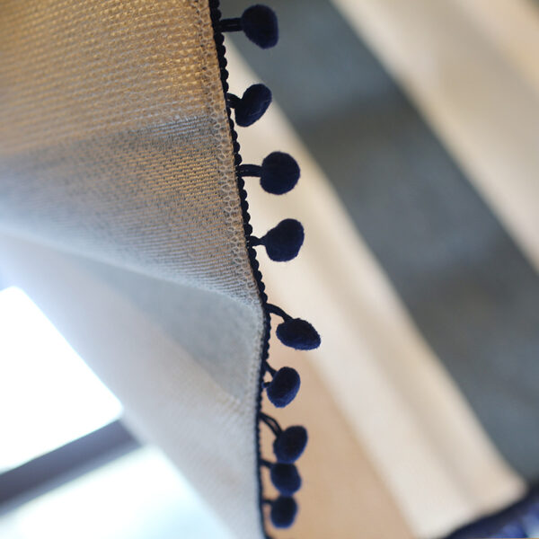 Close‑up view of black pom pom tassel edge on striped linen curtain panel