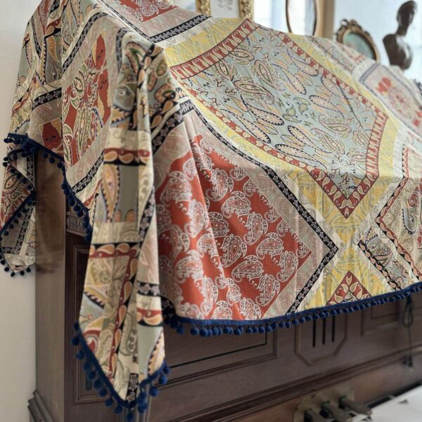 Vintage patchwork piano cover draped over upright piano, pom‑pom edge detail