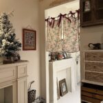 Soft rose print tie‑top curtain hanging on interior doorway, warm cottage‑style home decoration