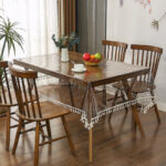 Clear lace‑trimmed vinyl table protector on farmhouse wooden dining table