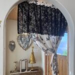 Timeless Parisian short curtain hanging over arched doorway, black lace top and cream floral curtain panel
