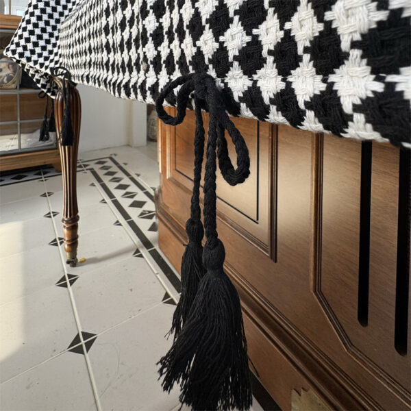 Close‑up of black tassel fringe detail on upright piano cover cloth, black‑white diamond‑check fabric