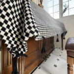 Side draping view of upright piano cover cloth, thick black‑white diamond‑check fabric with hanging tassels