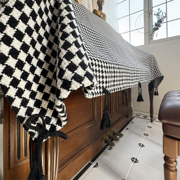 Side draping view of upright piano cover cloth, thick black‑white diamond‑check fabric with hanging tassels