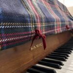 Close‑up view of red velvet bow decoration on vintage plaid piano top dust cover