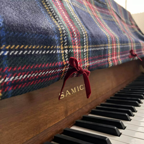 Close‑up view of red velvet bow decoration on vintage plaid piano top dust cover