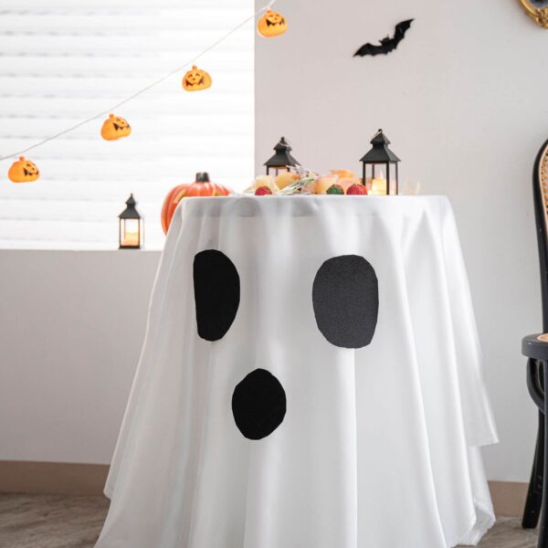 White Halloween ghost print round tablecloth styled on dessert table with pumpkin hanging banner