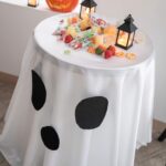 Close-up view of printed ghost face pattern on white round Halloween tablecloth for dessert display