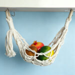 Cotton macrame holder fruit hammock hanging on blue tiled kitchen wall