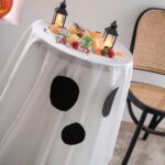 Side shot of flowy white polyester round tablecloth with ghost print for Halloween party decor