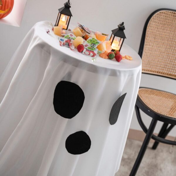 Side shot of flowy white polyester round tablecloth with ghost print for Halloween party decor